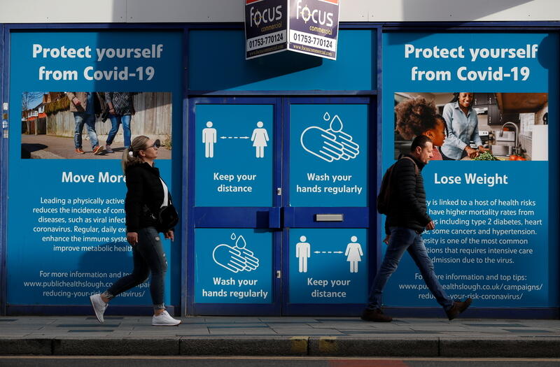 People walk past a signage about COVID-19 measures as the spread of the coronavirus disease (COVID-19) continues in Slough, Britain October 23, 2020. REUTERS/Paul Childs