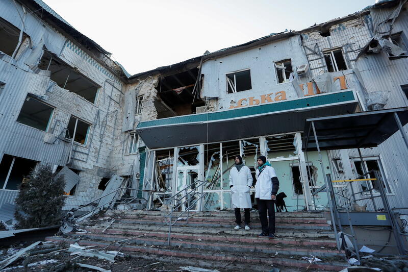 Two hospital staff members stand outside a destroyed hospital in Ukraine