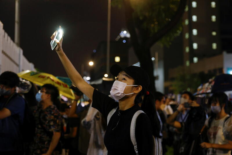 A supporter lights a torch light from her phone outside the headquarters of the Apple Daily newspaper, and its publisher Next Digital, after the announcement that the newspaper is folding its operations earlier, in Hong Kong, China June 23, 2021. REUTERS/Tyrone Siu