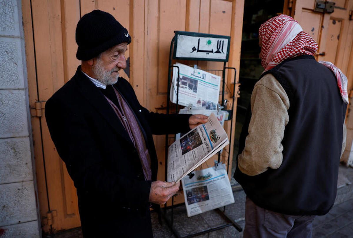 A Palestinian man reads a newspaper near closed shops, during a strike as a protest against the killing of senior Hamas official, Saleh al-Arouri, in Hebron in the Israeli-occupied West Bank January 3, 2024. REUTERS/Mussa Qawasma