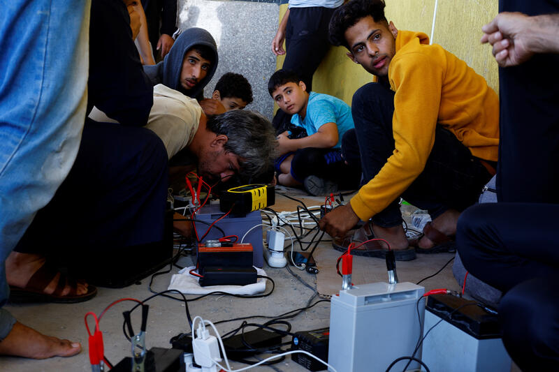 Palestinians charge their mobile phones from a point powered by solar panels provided by Adel Shaheen, an owner of an electric appliances shop, as electricity remains cut during the ongoing Israeli-Palestinian conflict, in Khan Younis in the southern Gaza Strip October 19, 2023.