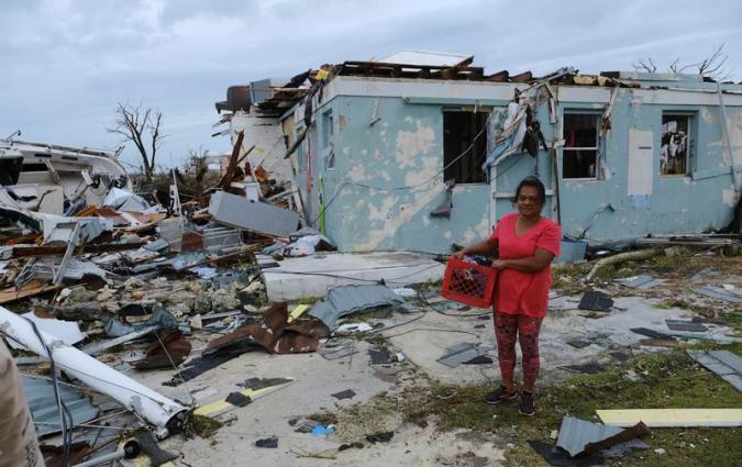 A woman poses for a photo near her damaged home in the aftermath of Hurricane Dorian