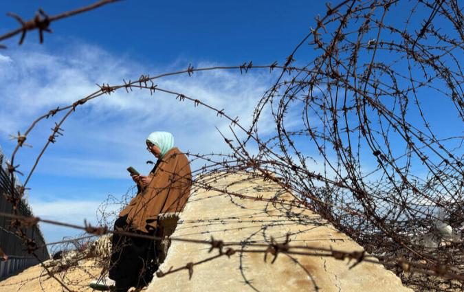 A displaced Palestinian woman tries to get internet service on her phone through the Egyptian networks to communicate with her relatives, near the border with Egypt, in Rafah in the southern Gaza Strip February 1, 2024.