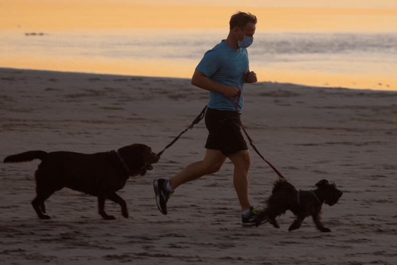 A man wears a face mask as he exercises with his dogs in Del Mar, California, U.S., December 1, 2020. REUTERS/Mike Blake