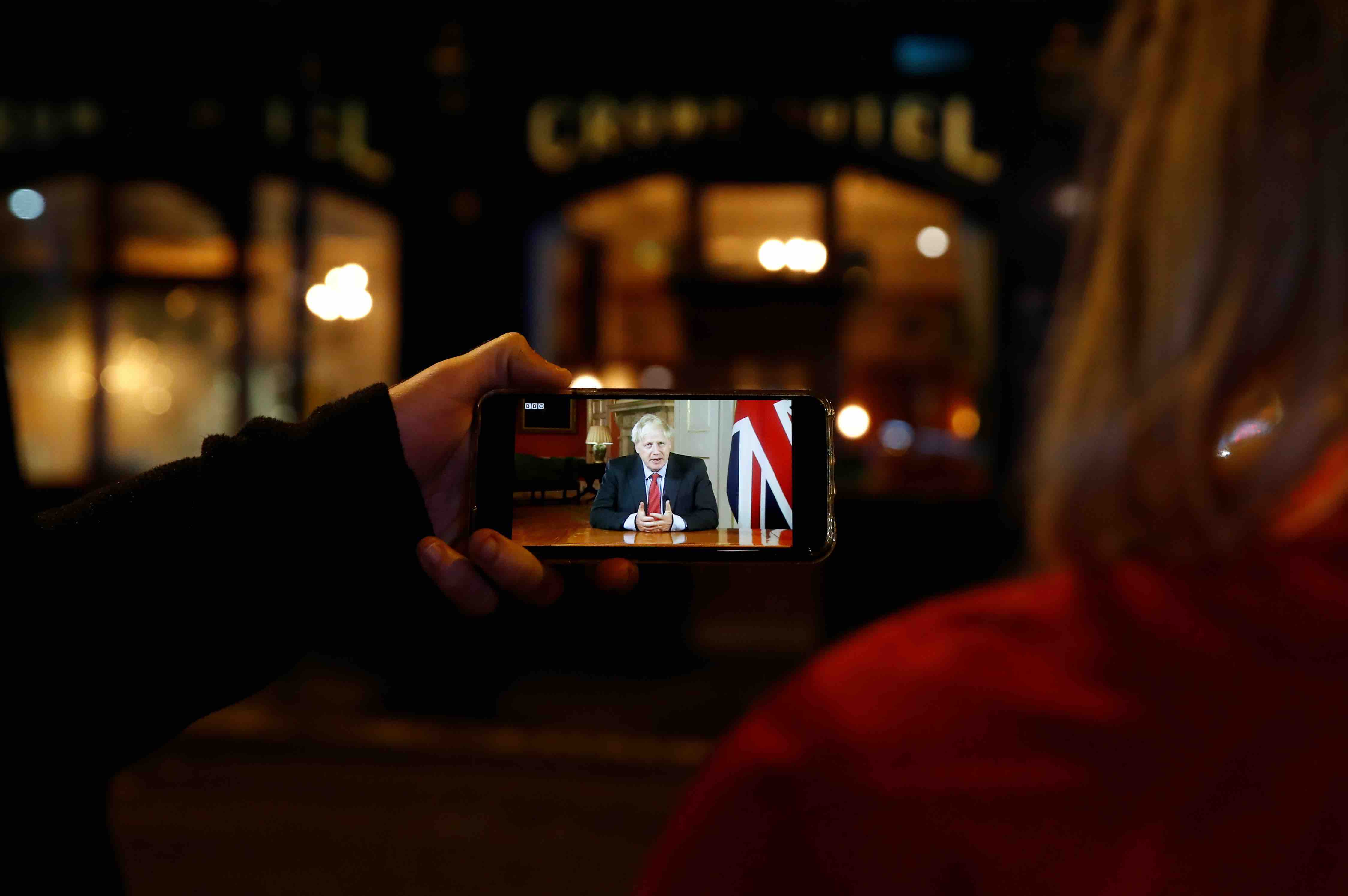 People watch the Prime Minister?s live address to the public on a mobile phone in Liverpool City Centre as Merseyside remains under lockdown due to the coronavirus disease (COVID-19) outbreak, in Liverpool, Britain September 22, 2020. REUTERS/Jason Cairnduff