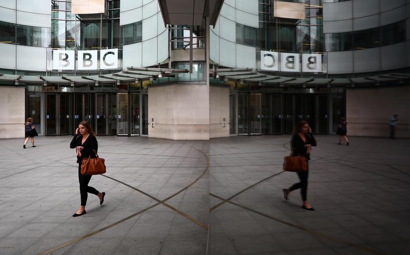 A woman is reflected as she passes the BBC's Broadcasting House in London, Britain July 19, 2017. REUTERS/Neil Hall
