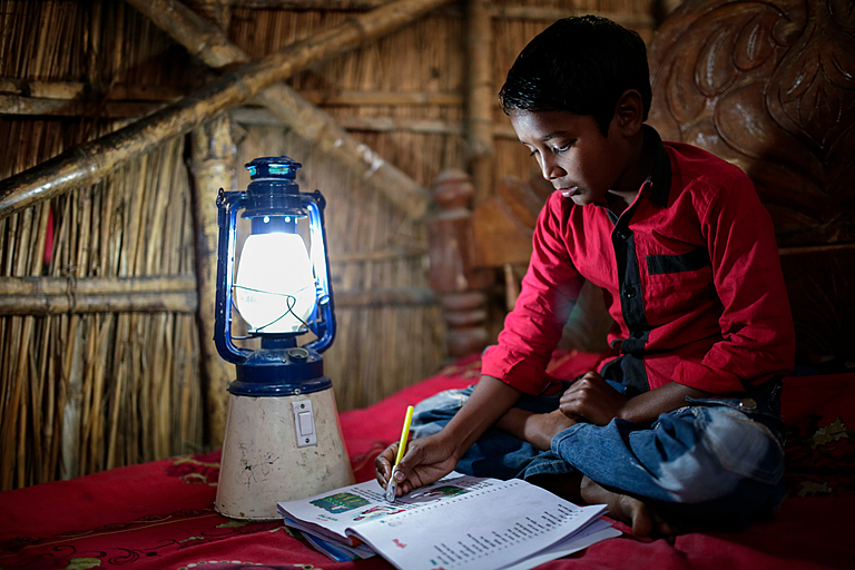 A child reads a book with the help of a solar lantern at his home, at Singra, Bangladesh. | Credit: Abir Abdullah | Climate Visuals