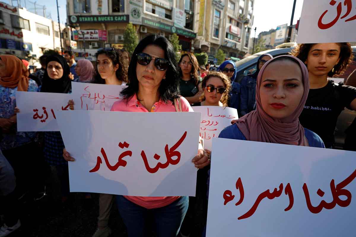 A crowd of demonstrators, in the foreground a woman wearing sunglasses and holding a placard with Arabic writing. Photo: Reuters/Mohamad Torokma