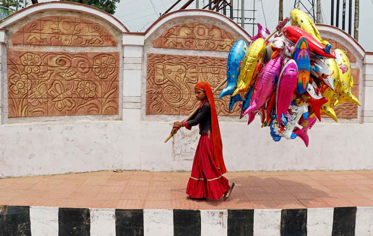 An Indian girl walks along a pavement with a high curb, carrying balloons. It is a representation of the need for curb cuts in Indian media. Photo: REUTERS/Jayanta Dey