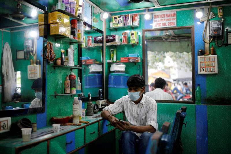 Um barbeiro olha pro seu celular, Delhi. Índia
