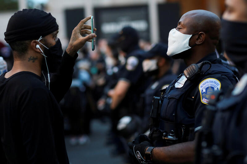 A demonstrator holds a mobile phone as he faces police officers near Black Lives Matter Plaza in Washington. REUTERS/Leah Millis