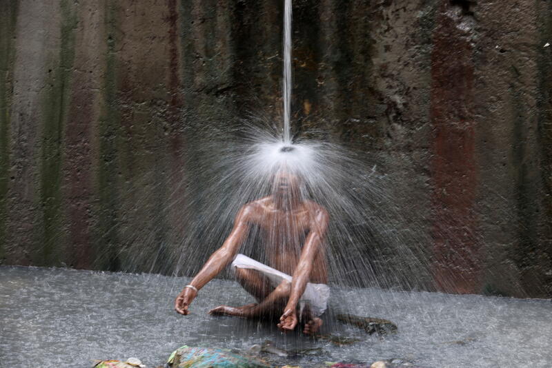 A man sits underneath a water pipe in New Delhi, India in 2022. 