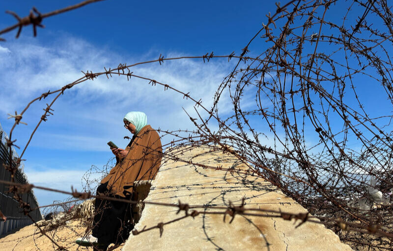 A displaced Palestinian woman tries to get internet service on her phone through the Egyptian networks to communicate with her relatives, near the border with Egypt, in Rafah in the southern Gaza Strip February 1, 2024.