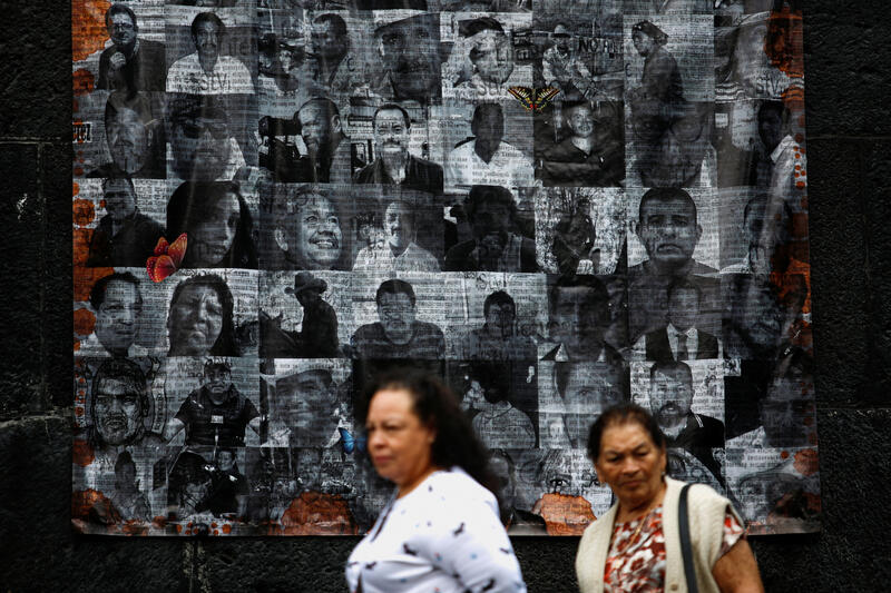 two woman walk past a memorial with black and white headshots of more than 40 journalists slain in Mexico