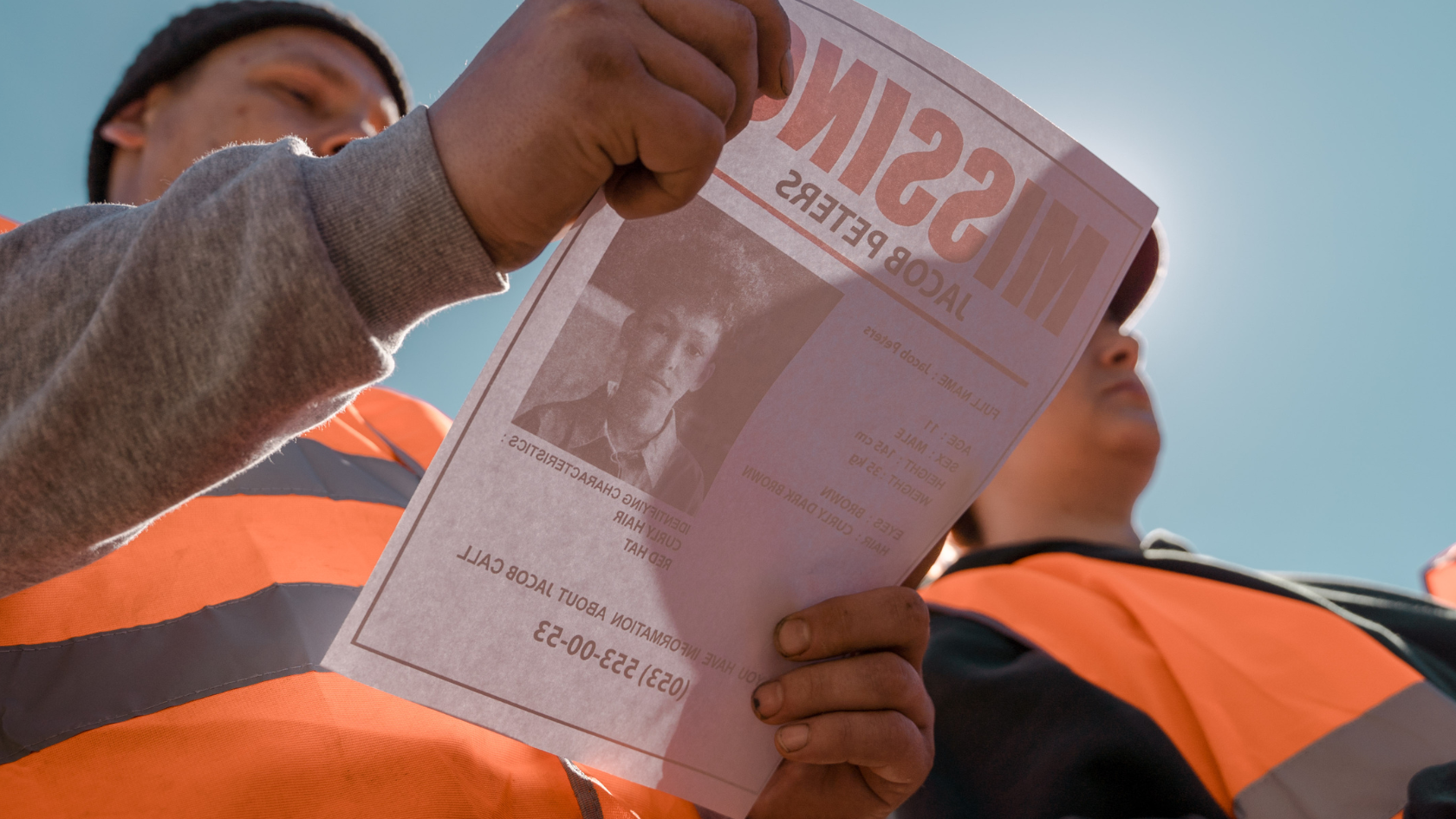 A man in a hi-vis jacket looks at a missing person flyer. 