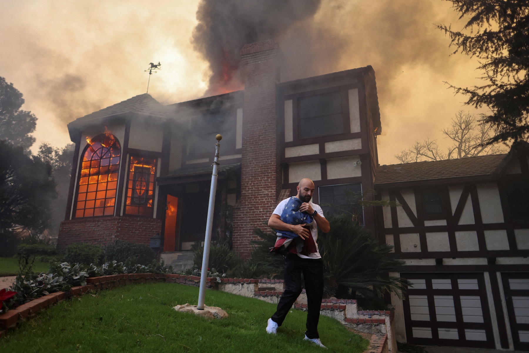 A person carrying a flag walks away from a burning house in Altadena, California. REUTERS/David Swanson