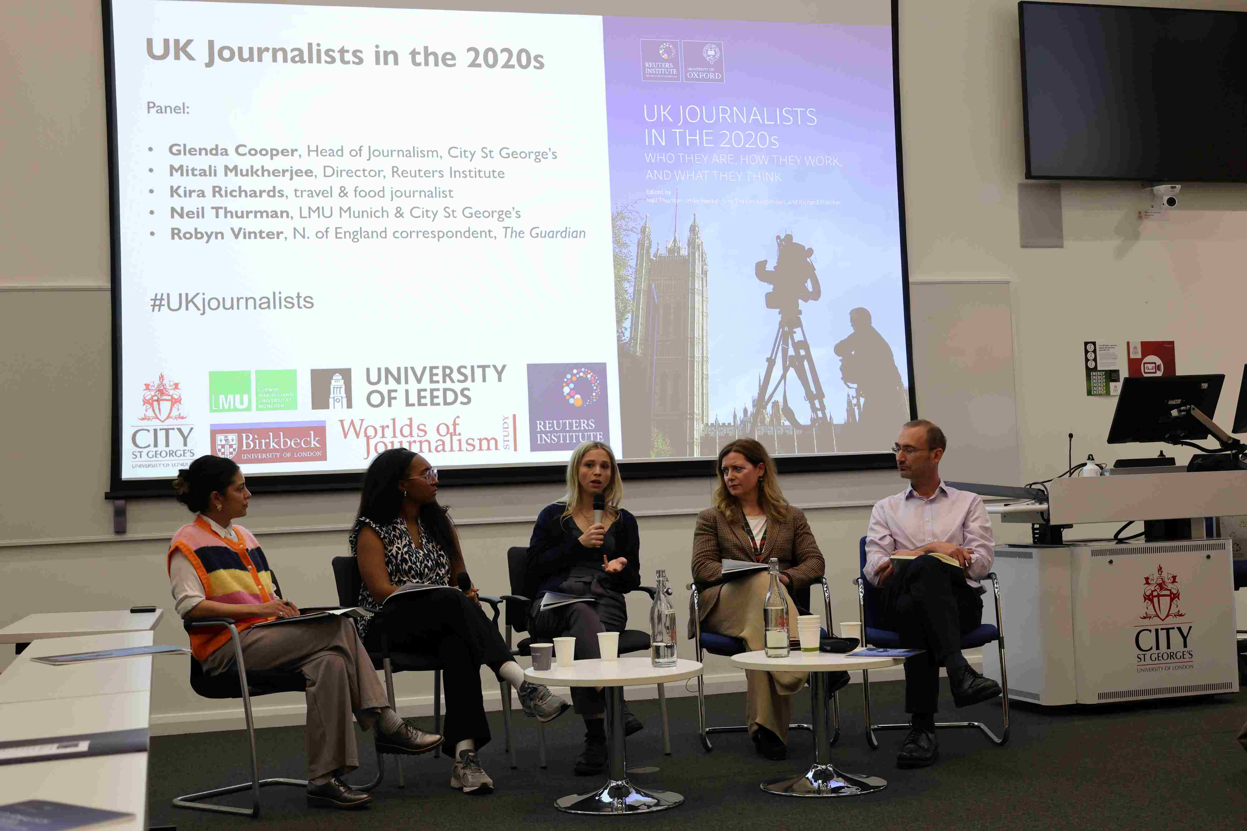 Five people sit in front of a screen displaying the text 'UK Journalists in the 2020s'. The woman sat in the middle of the group is holding a microphone.