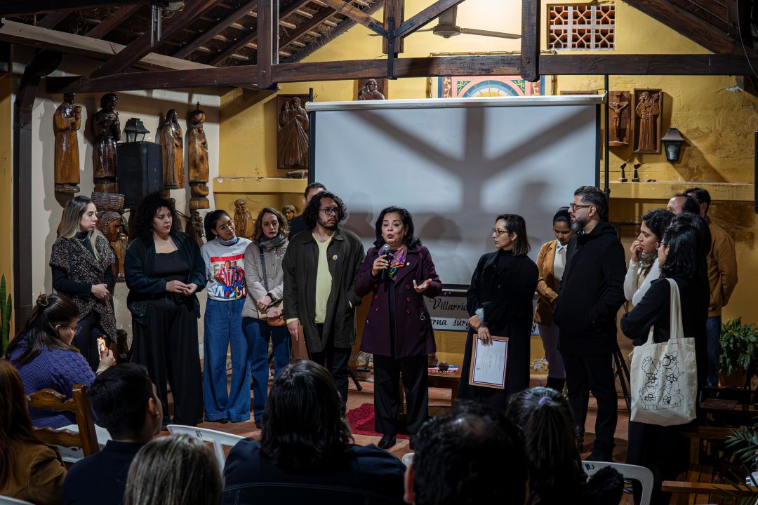 At the center, a neighbour stands with a microphone in front of a film screen with the staff of El Surtidor following the screening of a documentary about how a crypto farm was stopped. 