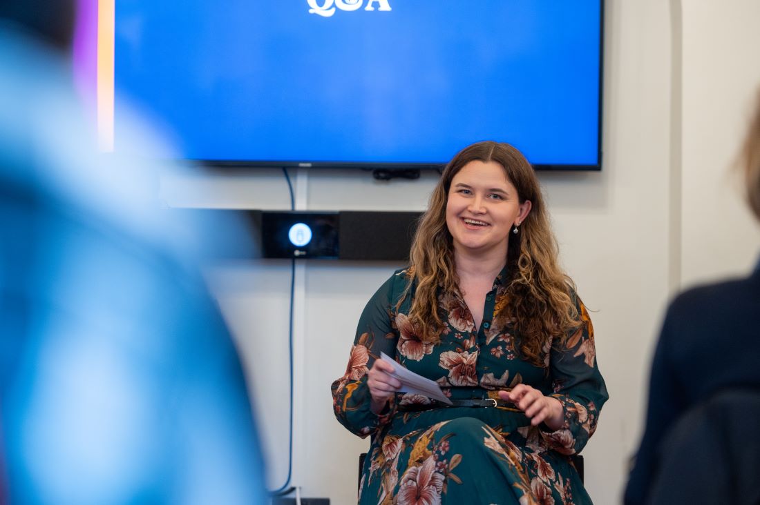 A woman in a floral dress smiles at an audience while presenting her findings at the Reuters Institute.