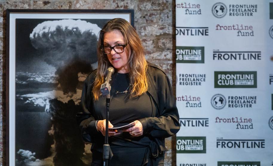 A woman in black glasses and dark clothing speaks into a microphone at the Frontline Club in London.