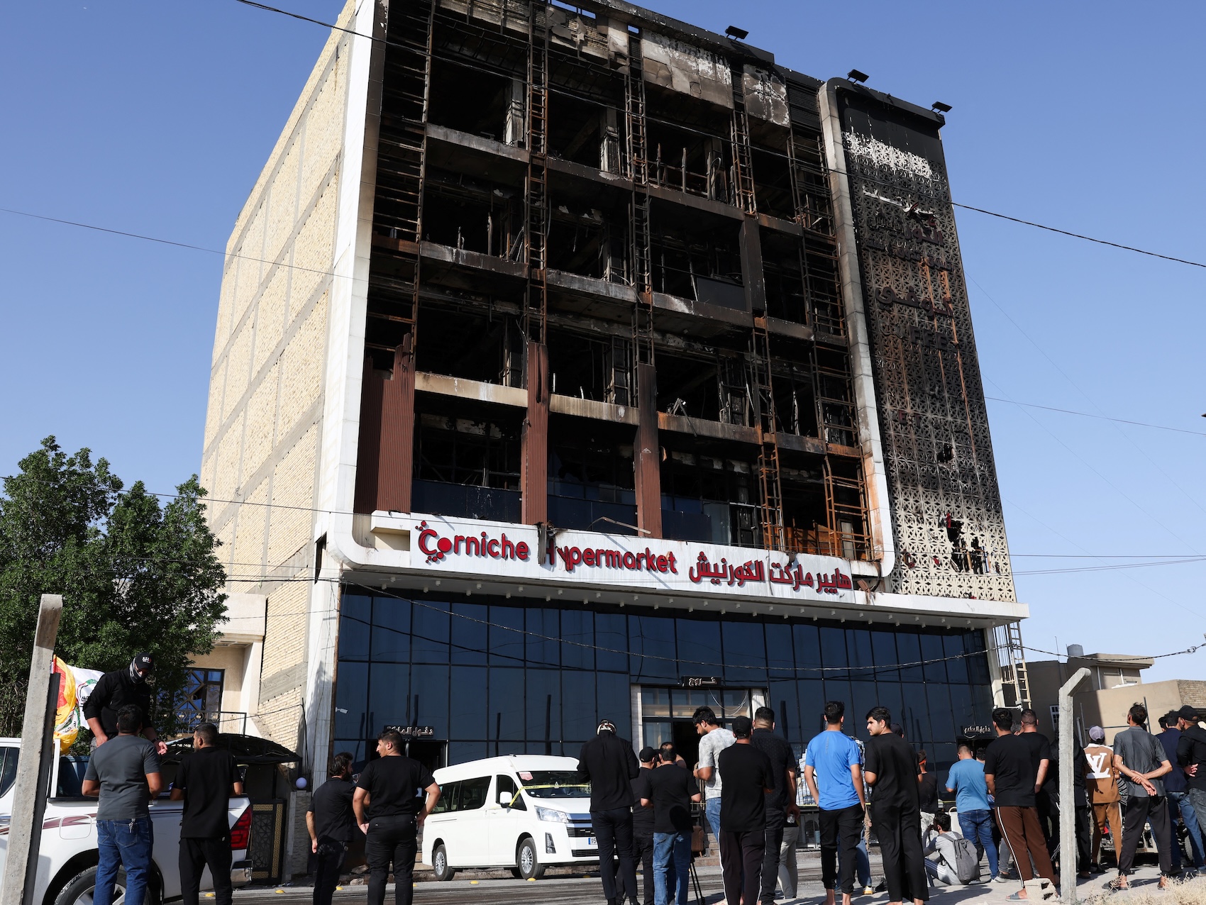 People gather next to a shopping center destroyed during a massive overnight fire that killed dozens of people, in Kut, Iraq on 17 July 2025. REUTERS/Ahmed Saad