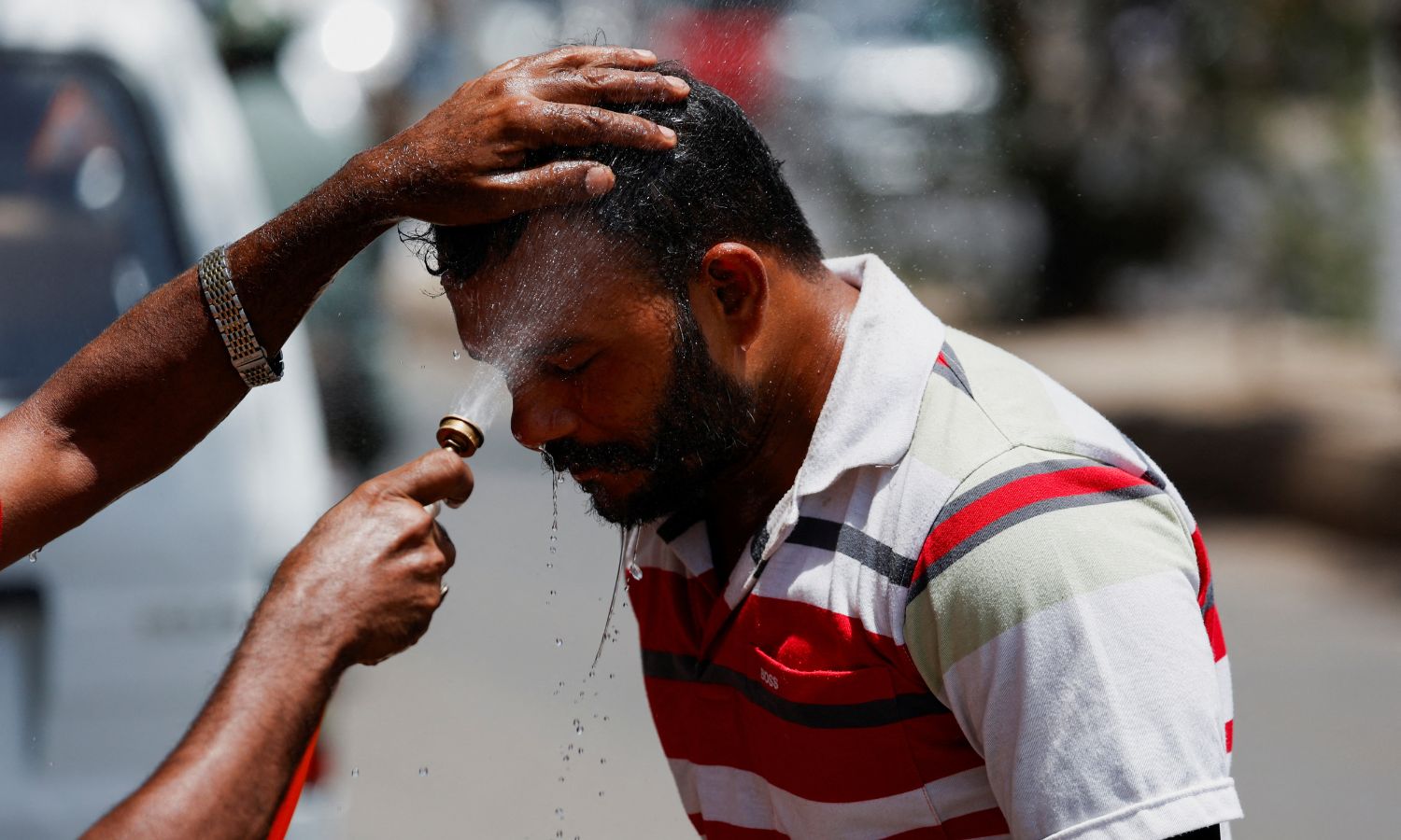 A man receives a spray of cold water to avoid heat during a hot day, along a road
