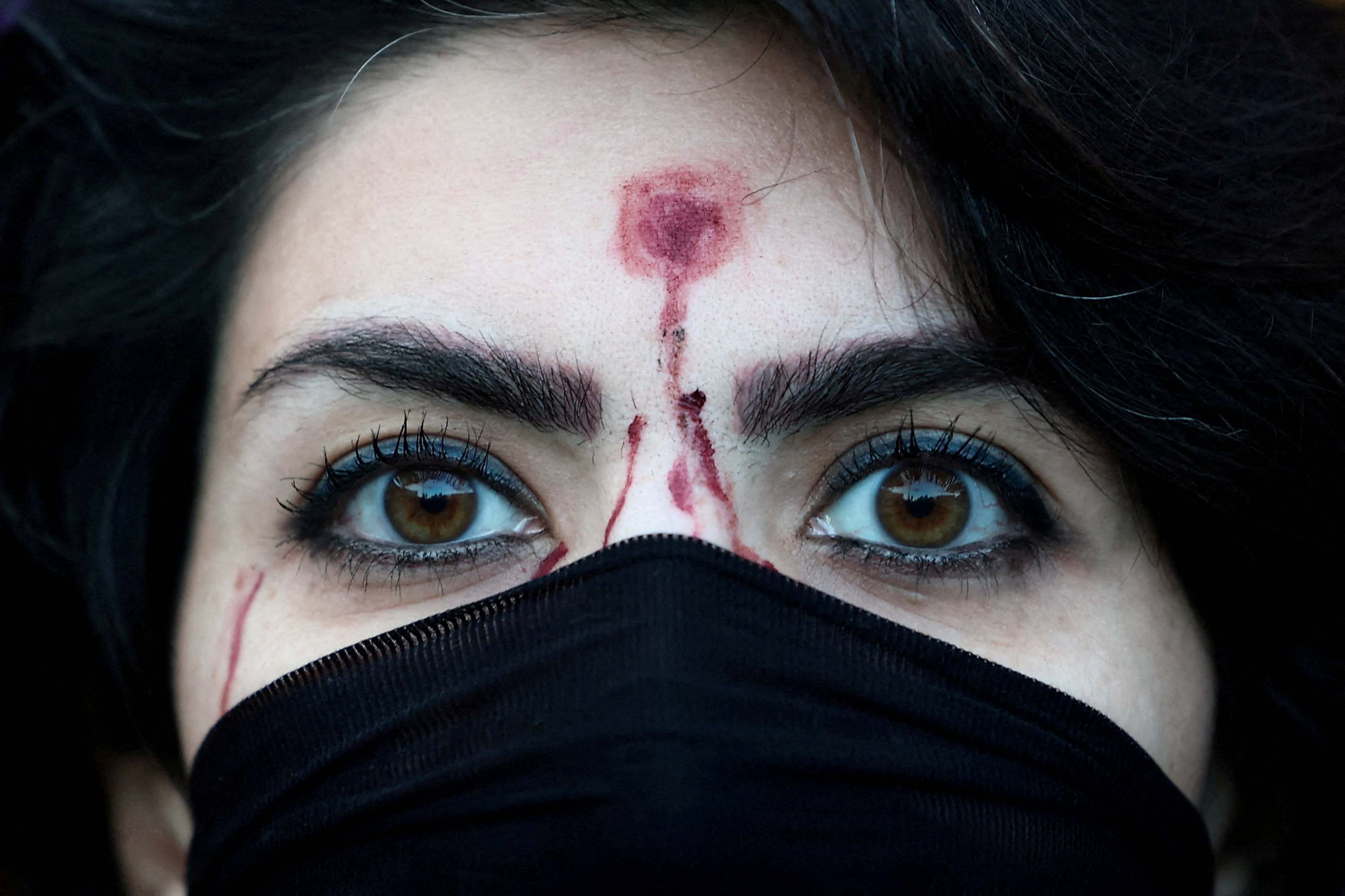 A woman with a mock-up of a gunshot bullet wound on her forehead.