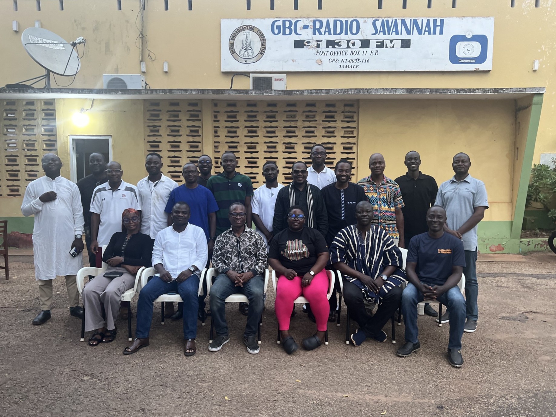 A group of people pose in front of a building with a sign identifying it as a radio station of the Ghana Broadcasting Corporation