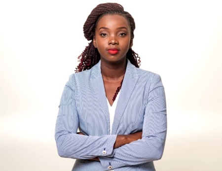 A professional photograph of a woman with her arms crossed in front of a light background.