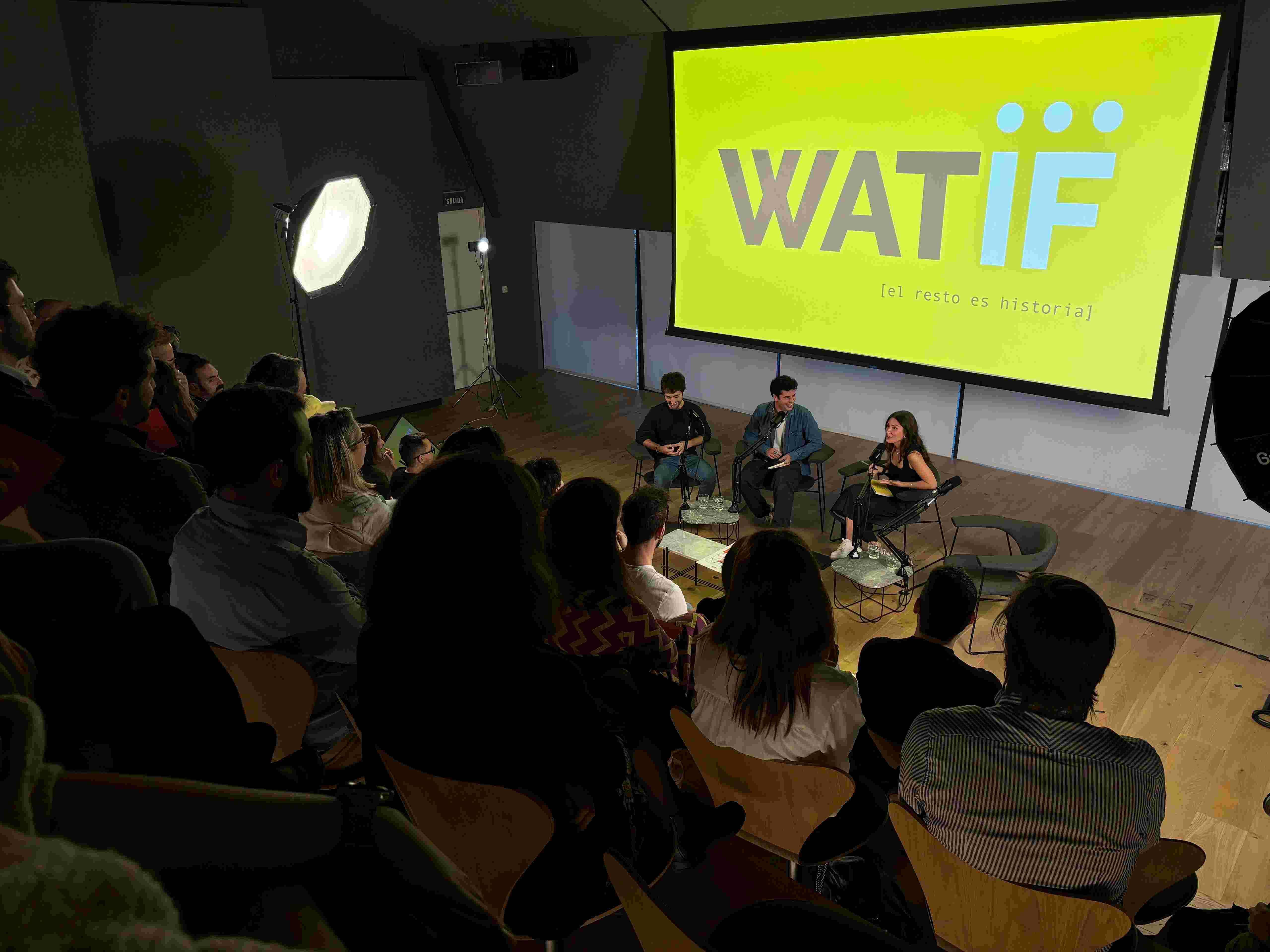 A view from above of three people talking on a stage in a theatre. 