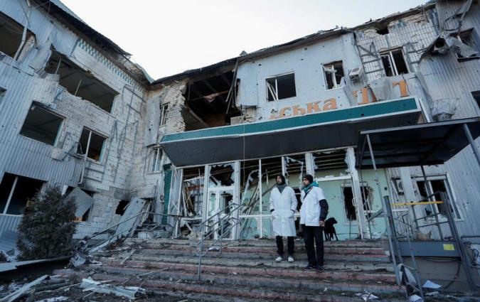 Two hospital staff members stand outside a destroyed hospital in Ukraine