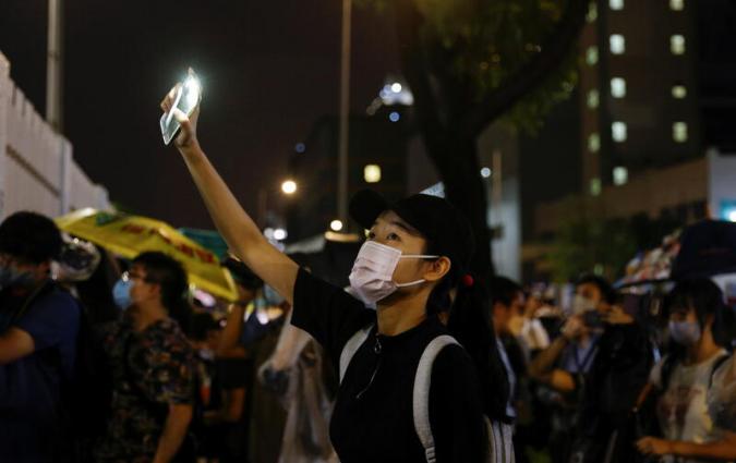 A supporter lights a torch light from her phone outside the headquarters of the Apple Daily newspaper, and its publisher Next Digital, after the announcement that the newspaper is folding its operations earlier, in Hong Kong, China June 23, 2021. REUTERS/Tyrone Siu