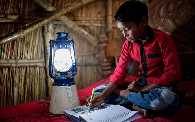 A child reads a book with the help of a solar lantern at his home, at Singra, Bangladesh. | Credit: Abir Abdullah | Climate Visuals