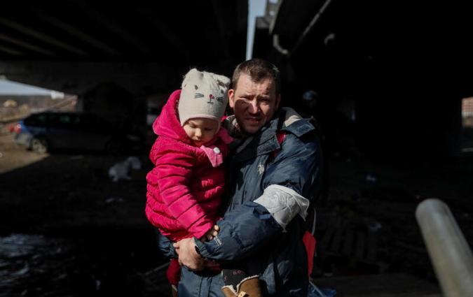 A man and a toddler cross the Irpin river under a destroyed bridge in early March 2022. REUTERS/Gleb Garanich