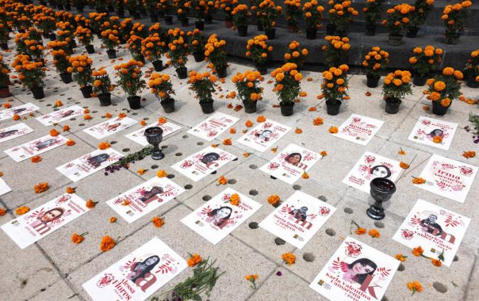 Posters with pictures of people are placed on the floor in front of rows of orange flowers.