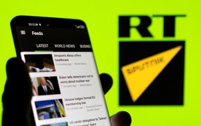 La app de RT en un teléfono móvil delante de los logos de RT y Sputnik. REUTERS/Dado Ruvic/Ilustración