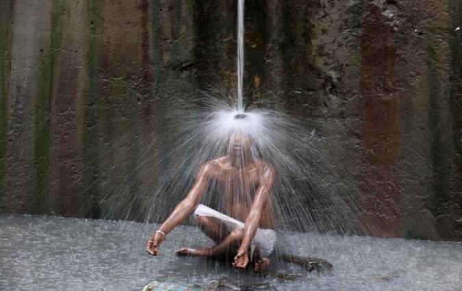 A man sits underneath a water pipe in New Delhi, India in 2022. 