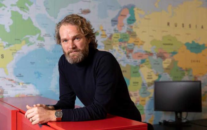 Ton rests against a cabinet in his office, with a world map behind him. Photo: Henriette Guest