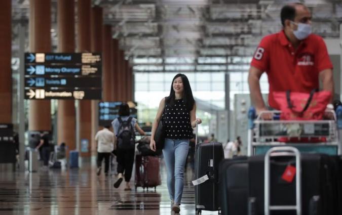 Clara walks through an airport with her suitcase. 
