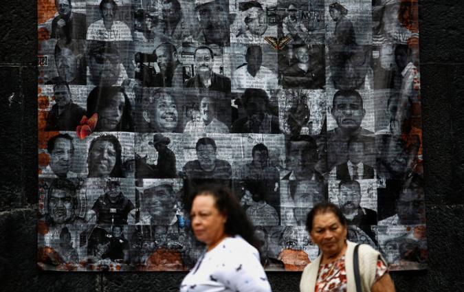 two woman walk past a memorial with black and white headshots of more than 40 journalists slain in Mexico