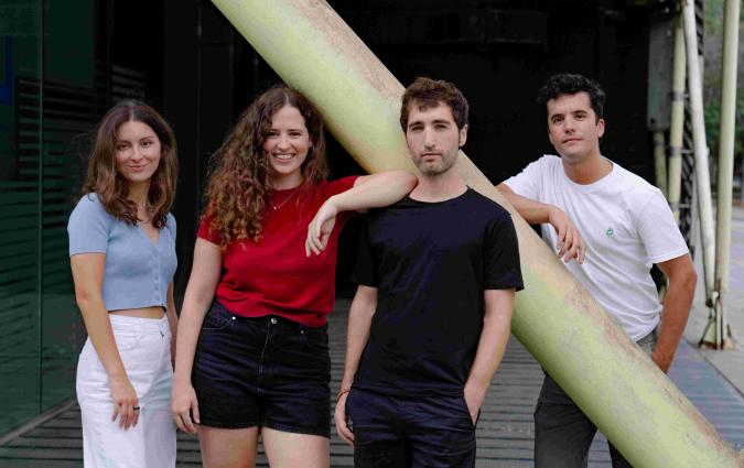 Four young people pose smiling in front of a building.