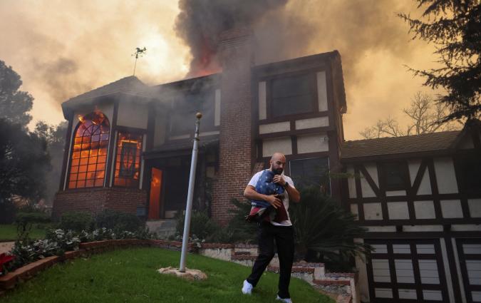 A person carrying a flag walks away from a burning house in Altadena, California. REUTERS/David Swanson