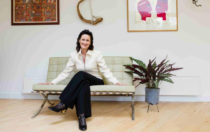 Emily Kasriel sits on a small sofa in what appears to be a living room.