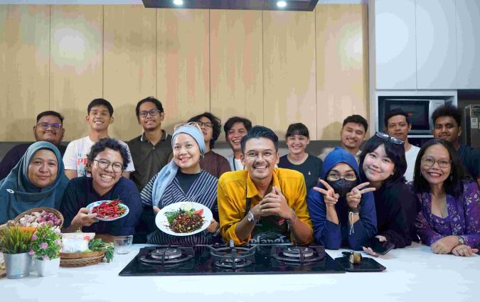 A group of people huddle in a kitchen posing for a picture. Three people on the left-hand side are holding plates of food.
