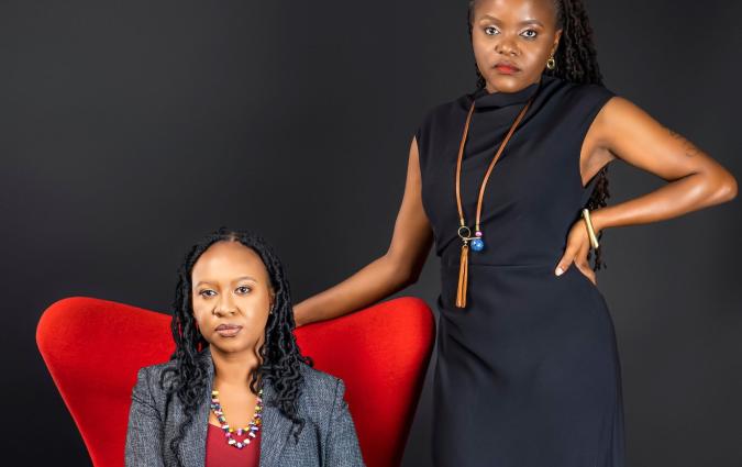 A photograph of two women, one sitting on a red armchair, and the other standing beside her with her arm across the back of the chair.