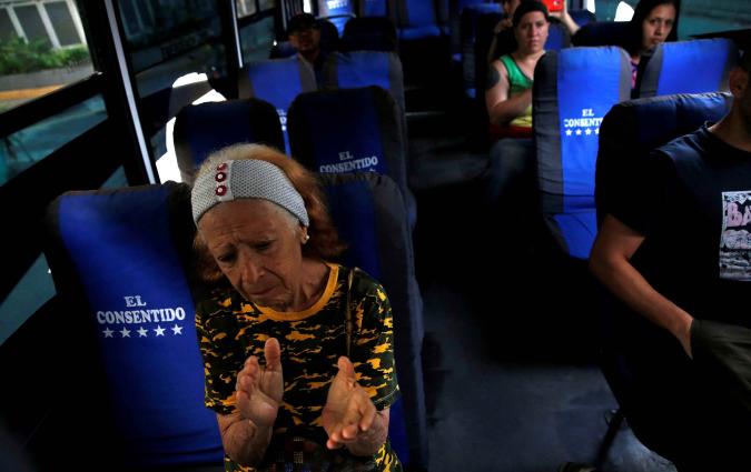 A woman seated in a bus applauds.