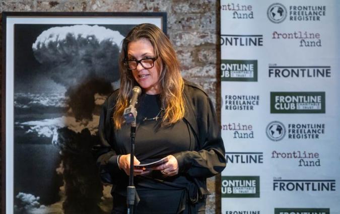A woman in black glasses and dark clothing speaks into a microphone at the Frontline Club in London.