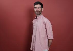Francesco Zaffarano stands in front of a deep red background in a half profile with his arms crossed behind his back.