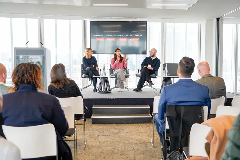 A photograph of three people on a stage in front of a room full of people.