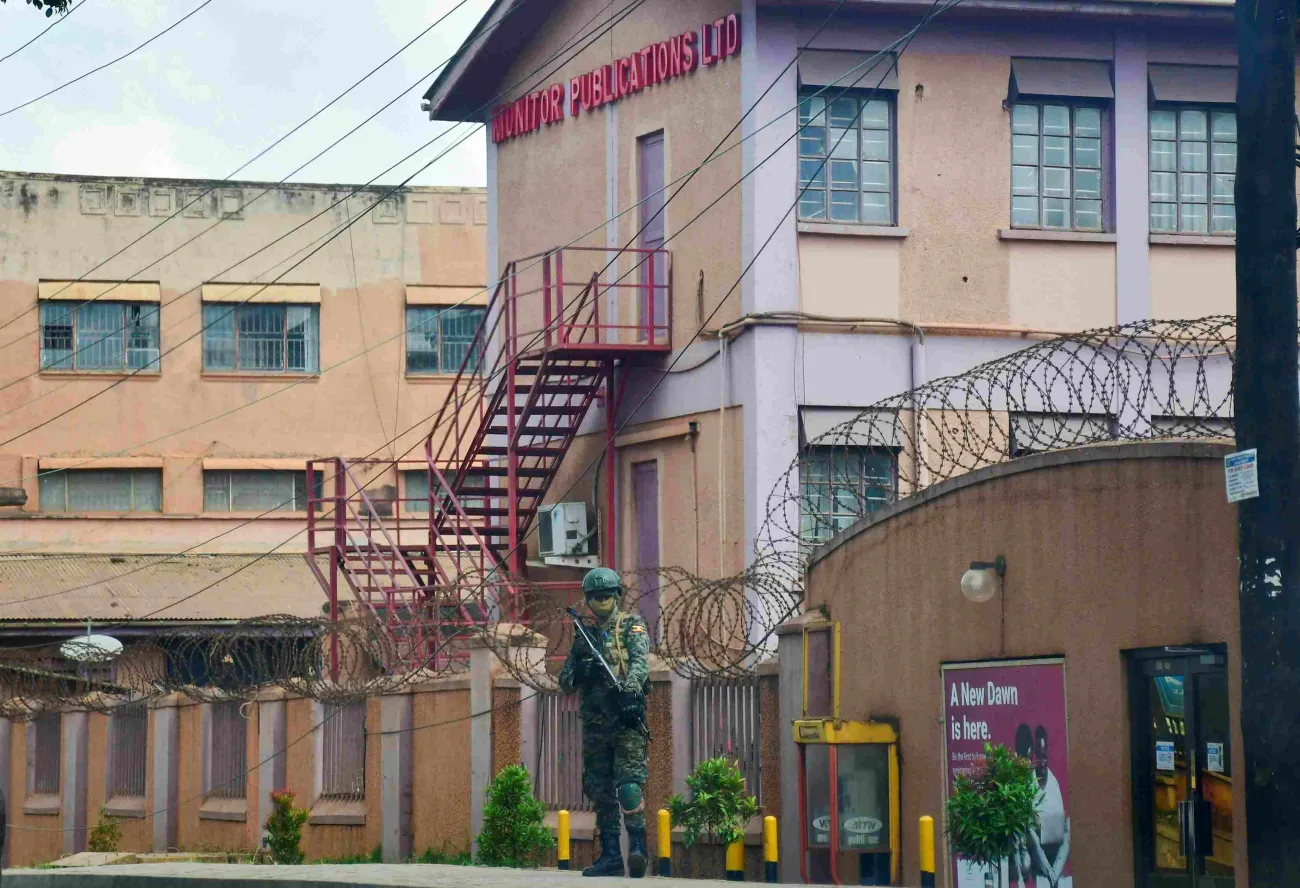 A soldier stands outside the barbed-wire perimeter of the Monitor Publications Ltd building, with the company sign visible above.